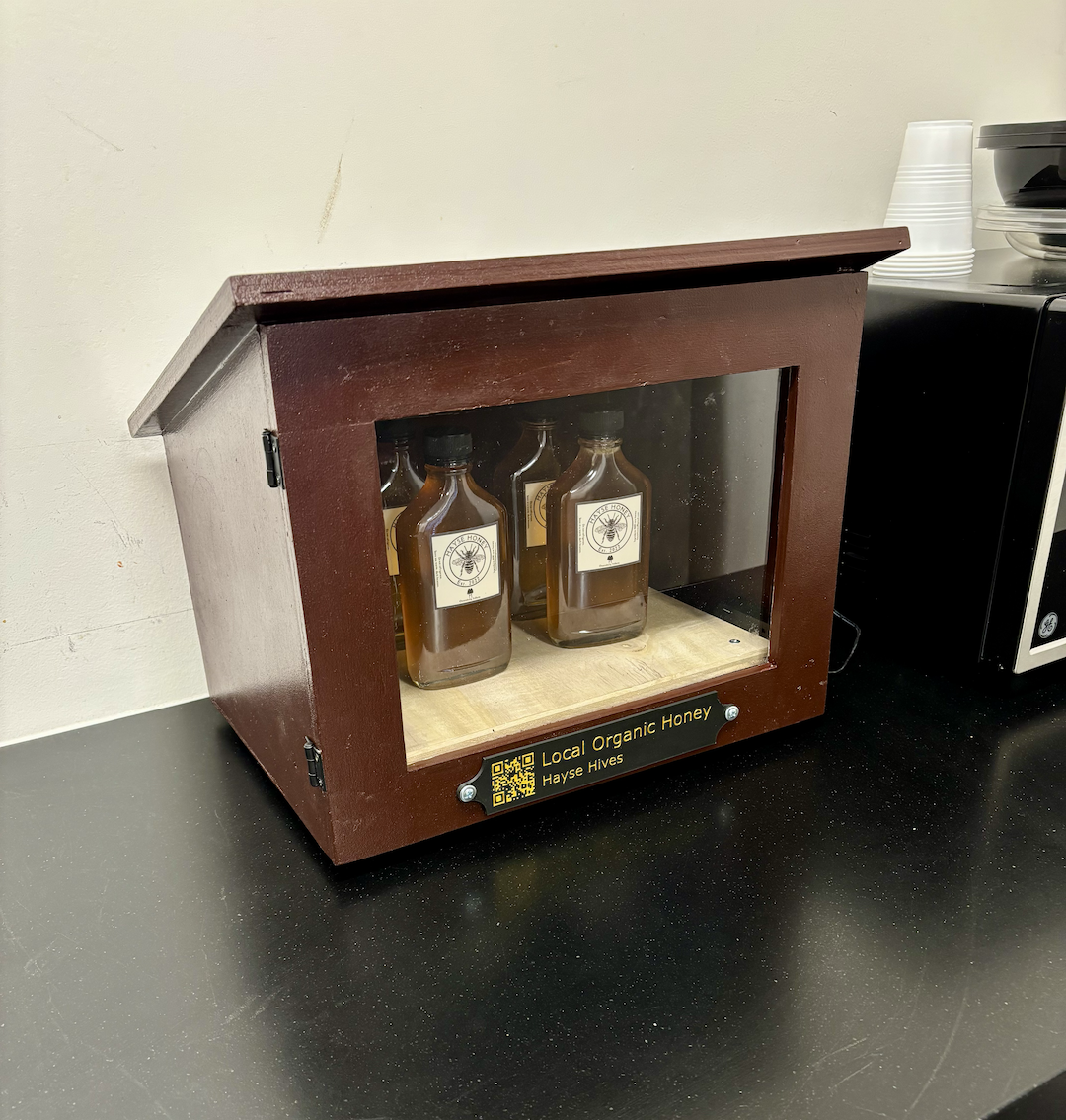Hayse Hives' wooden honey cabinet with jars of local honey behind a glass door and a QR code on the front